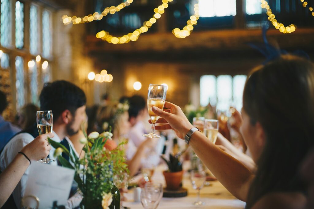結婚式披露宴でゲストがシャンパングラスを持ち乾杯する写真｜温かみのあるライトと装花が印象的なテーブル席
