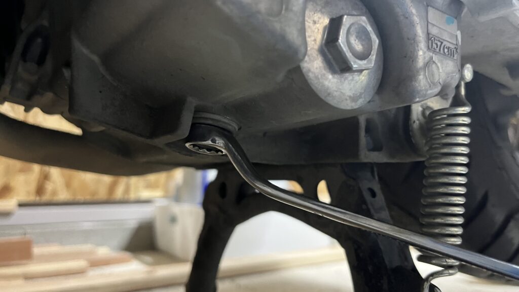 PCX160のオイルドレンボルトをレンチで緩めている作業中の写真