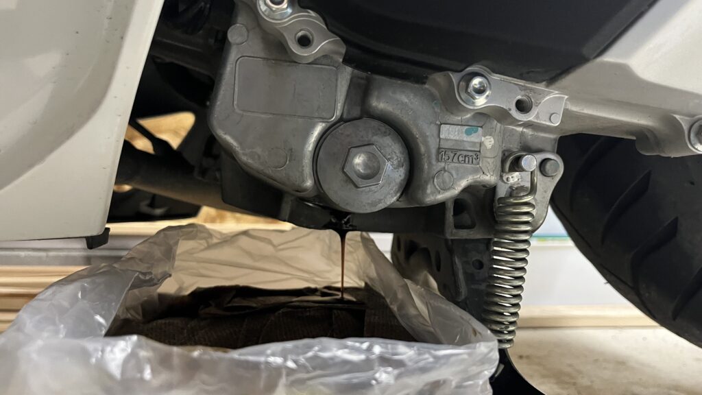PCX160のオイル交換作業でドレンから古いエンジンオイルを排出している場面