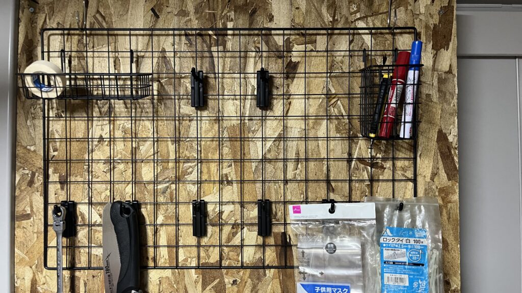 合板の壁にワイヤーメッシュを固定し、工具やマーカーペン、小物類を吊るして収納している完成状態の写真