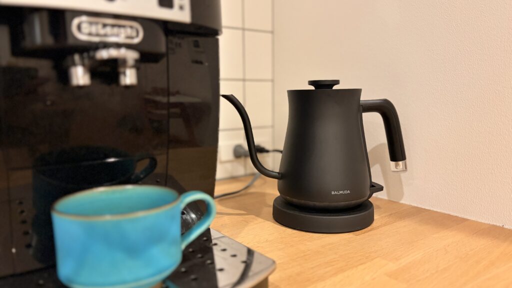 キッチンに置かれたBALMUDAの黒い電気ケトルと青いカップ、背後にはエスプレッソマシンが見える