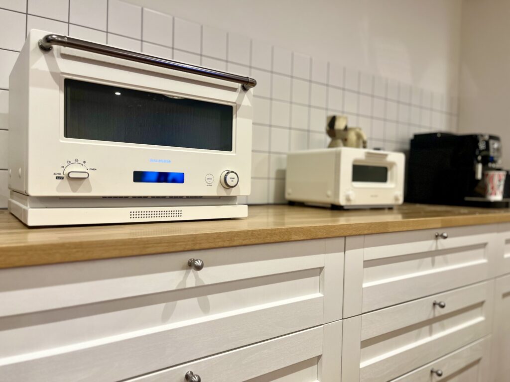 白を基調としたキッチンに設置されたバルミューダのオーブンレンジ。木製カウンターとタイル壁に調和し、おしゃれな雰囲気を演出している。